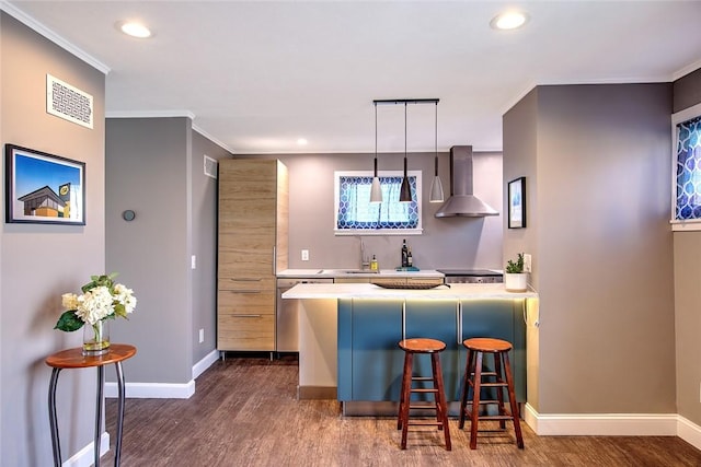 kitchen featuring a kitchen bar, wall chimney exhaust hood, decorative light fixtures, crown molding, and sink