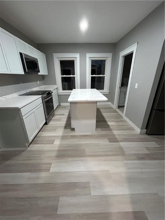 kitchen featuring white cabinets, light wood-type flooring, stainless steel appliances, and a kitchen island