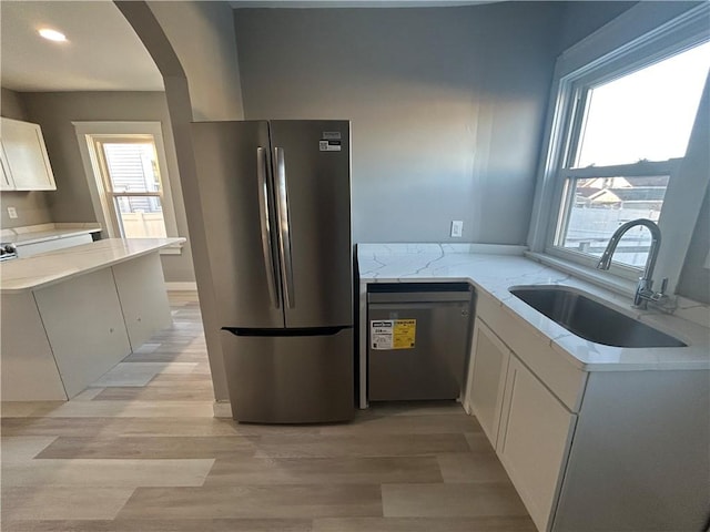 kitchen with dishwasher, sink, stainless steel refrigerator, white cabinetry, and light stone countertops