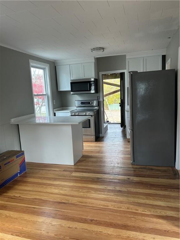 kitchen with white cabinets, kitchen peninsula, stainless steel appliances, and light hardwood / wood-style floors