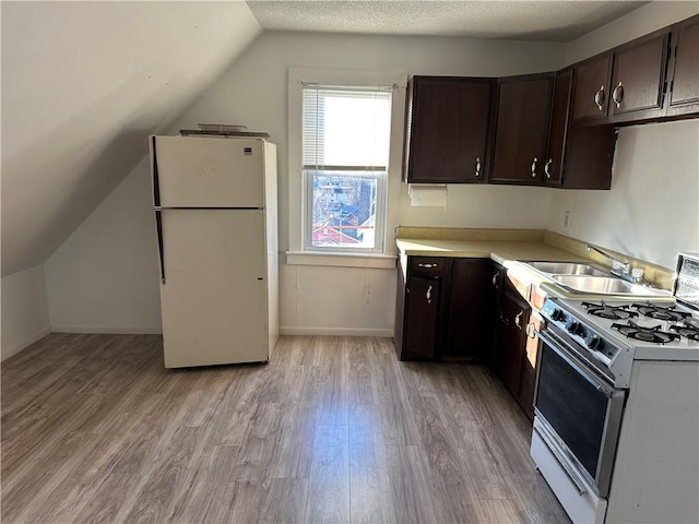 kitchen with vaulted ceiling, sink, white appliances, dark brown cabinetry, and light wood-type flooring