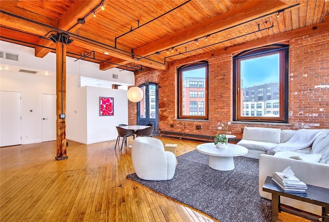 living room featuring brick wall, beam ceiling, track lighting, and hardwood / wood-style flooring