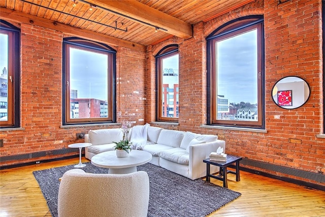 living room with wood ceiling, hardwood / wood-style flooring, track lighting, brick wall, and beam ceiling