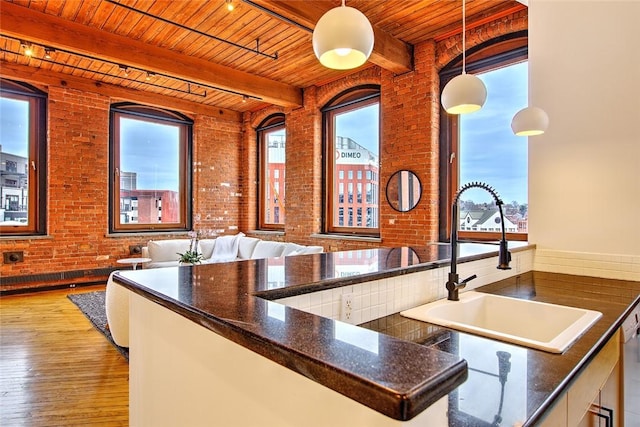 kitchen with brick wall, wood ceiling, decorative light fixtures, a healthy amount of sunlight, and beam ceiling