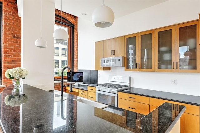 kitchen featuring decorative light fixtures, brick wall, dark stone countertops, and white appliances