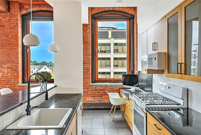 kitchen featuring light tile patterned floors, brick wall, sink, and white appliances