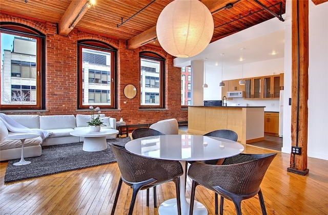 dining room featuring brick wall, a wealth of natural light, wooden ceiling, light hardwood / wood-style flooring, and beam ceiling