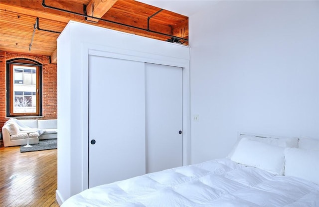 bedroom with beamed ceiling, hardwood / wood-style flooring, wood ceiling, a closet, and brick wall