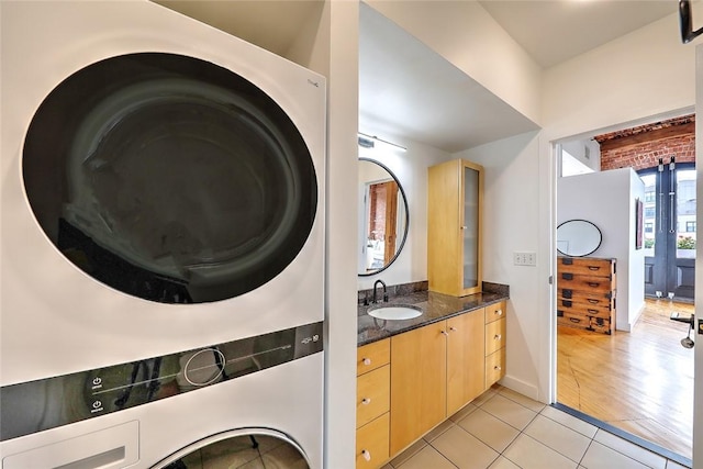 laundry area featuring sink, light tile patterned floors, and stacked washer and clothes dryer