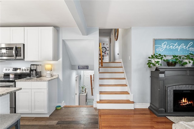 staircase featuring a tiled fireplace, hardwood / wood-style flooring, and beamed ceiling