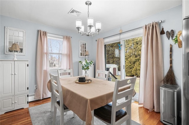 dining space with hardwood / wood-style floors, a baseboard heating unit, a wealth of natural light, and a notable chandelier