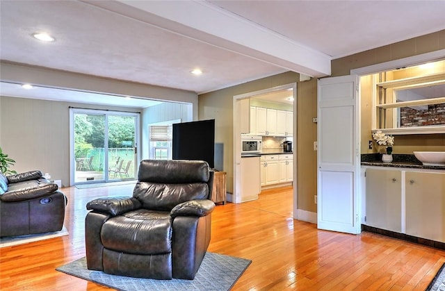 living room featuring light wood-type flooring, beamed ceiling, and sink