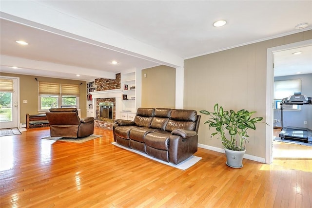 living room featuring built in shelves, a brick fireplace, and light hardwood / wood-style floors