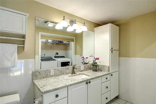 bathroom featuring washer and clothes dryer, tile patterned flooring, vanity, tile walls, and toilet