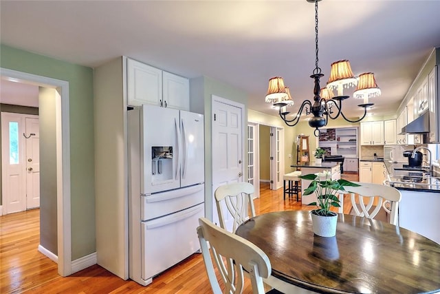 dining space featuring light wood-type flooring, sink, and an inviting chandelier