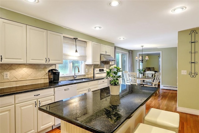 kitchen featuring decorative light fixtures, a center island, sink, white cabinets, and dark stone counters