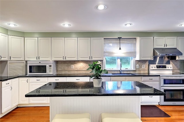 kitchen with white cabinetry, a breakfast bar area, range with two ovens, a kitchen island, and sink