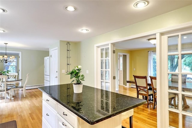 kitchen featuring decorative light fixtures, dark stone countertops, a kitchen island, white cabinetry, and light wood-type flooring