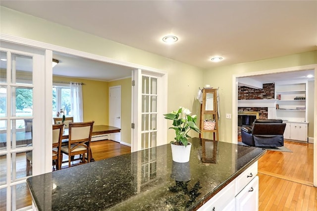 kitchen with white cabinetry, dark stone countertops, a fireplace, and hardwood / wood-style flooring