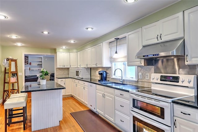 kitchen with white cabinetry, decorative light fixtures, a kitchen breakfast bar, white appliances, and sink