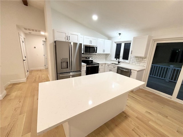 kitchen featuring lofted ceiling, backsplash, appliances with stainless steel finishes, and white cabinetry