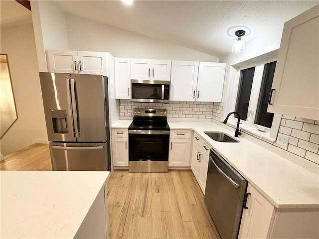 kitchen featuring white cabinetry, stainless steel appliances, backsplash, vaulted ceiling, and sink