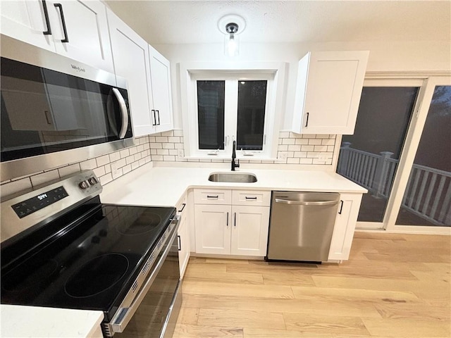 kitchen featuring white cabinets, appliances with stainless steel finishes, tasteful backsplash, light hardwood / wood-style floors, and sink