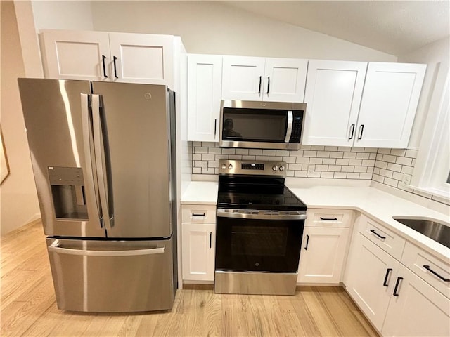 kitchen with white cabinetry, stainless steel appliances, tasteful backsplash, vaulted ceiling, and light hardwood / wood-style flooring