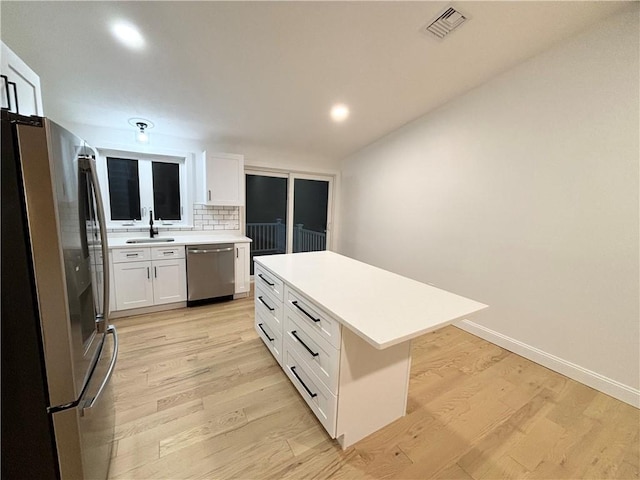 kitchen featuring a center island, white cabinetry, stainless steel appliances, decorative backsplash, and light wood-type flooring