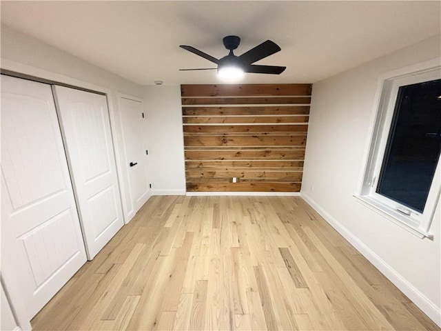 unfurnished bedroom featuring ceiling fan, light hardwood / wood-style floors, a closet, and wood walls