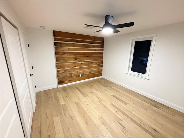 unfurnished bedroom with ceiling fan, light wood-type flooring, and wooden walls