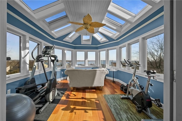 exercise room with wood-type flooring, vaulted ceiling with skylight, a wealth of natural light, and ceiling fan