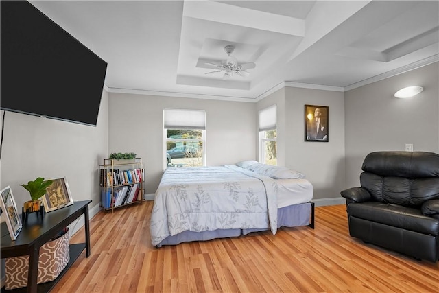 bedroom with light wood-type flooring, ceiling fan, ornamental molding, and a raised ceiling