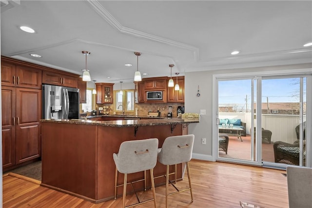 kitchen with dark stone countertops, light hardwood / wood-style floors, pendant lighting, crown molding, and stainless steel appliances