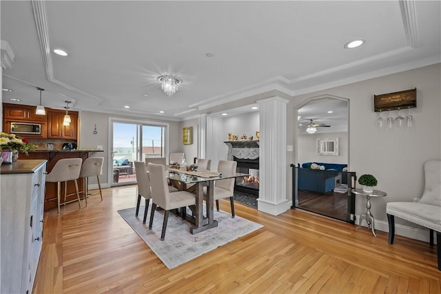 dining space with ceiling fan, a multi sided fireplace, ornamental molding, and light hardwood / wood-style floors