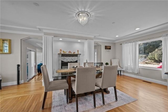 dining room with a notable chandelier, crown molding, light wood-type flooring, a high end fireplace, and ornate columns