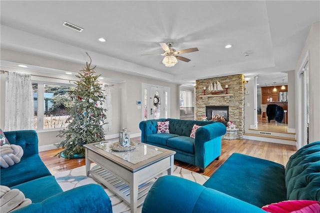 living room with light hardwood / wood-style floors, a raised ceiling, and a stone fireplace