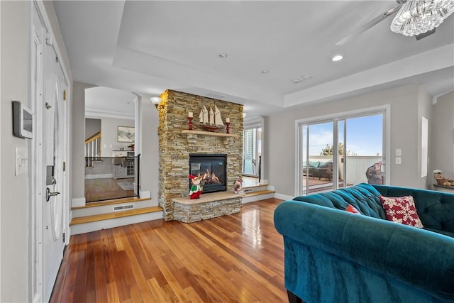 living room featuring a raised ceiling, a stone fireplace, and hardwood / wood-style floors