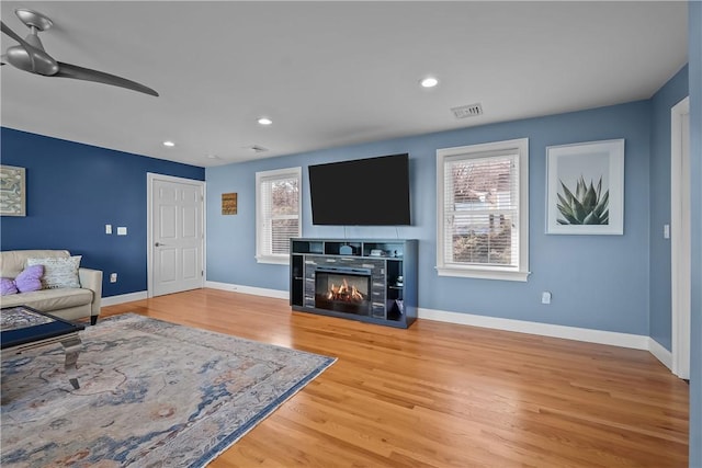 living room featuring ceiling fan, hardwood / wood-style floors, and a tiled fireplace