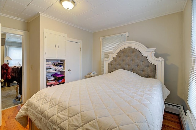 bedroom with a baseboard radiator, hardwood / wood-style floors, a closet, and ornamental molding