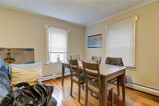 dining space featuring a baseboard heating unit, ornamental molding, and light wood-type flooring