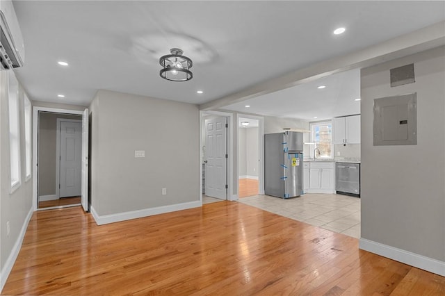 unfurnished living room featuring light wood-type flooring, an AC wall unit, sink, and electric panel