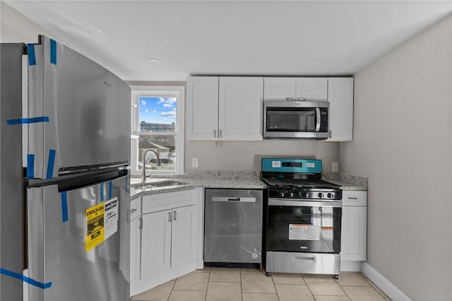 kitchen with appliances with stainless steel finishes, sink, white cabinetry, and light tile patterned flooring