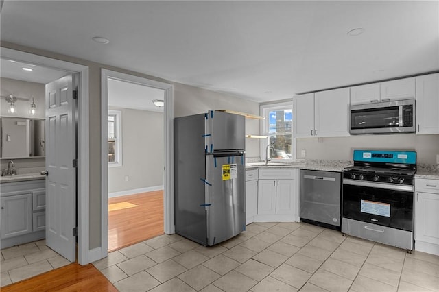 kitchen with sink, light tile patterned flooring, white cabinetry, light stone countertops, and appliances with stainless steel finishes