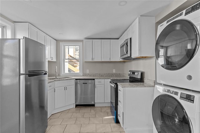 kitchen featuring stacked washer / drying machine, sink, light stone countertops, stainless steel appliances, and white cabinets