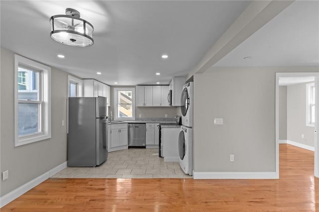 kitchen with light wood-type flooring, appliances with stainless steel finishes, stacked washer and clothes dryer, and white cabinetry