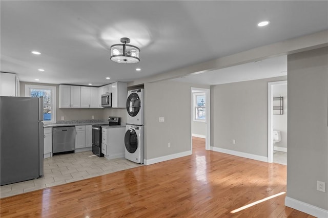 kitchen featuring stacked washing maching and dryer, light hardwood / wood-style floors, stainless steel appliances, and white cabinetry