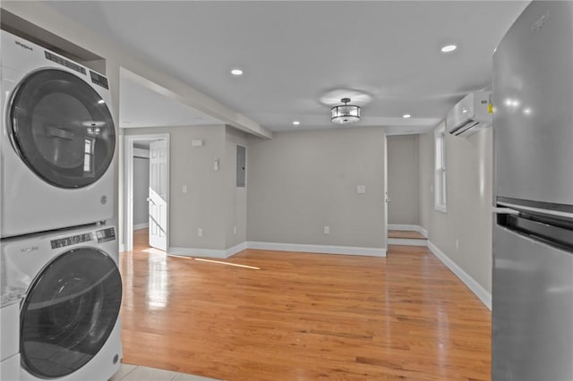 clothes washing area with a wall mounted AC, stacked washer and dryer, and light hardwood / wood-style flooring