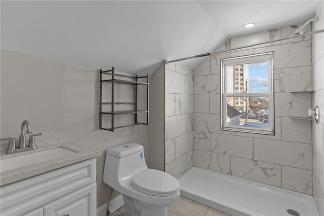 bathroom with toilet, tiled shower, tile patterned flooring, lofted ceiling, and vanity