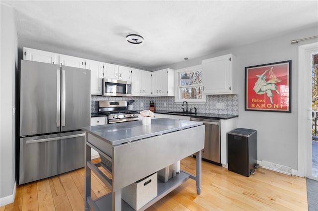 kitchen with sink, white cabinetry, hanging light fixtures, light wood-type flooring, and appliances with stainless steel finishes